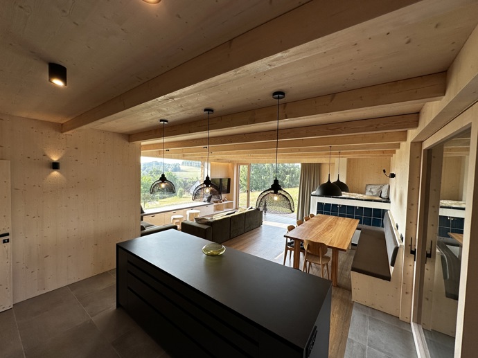 Přírodní minimalistický design a decentní barevná paleta zajišťuje dokonalou eleganci. Velkými okny proudí dovnitř mnoho světla, přes které je možné pozorovat malebnou krajinu, která celou chatu obklopuje. Fasádu domu tvoří ručně štípané modřínový šindel, zatímco uvnitř je obloženo smrkovými biodeskami.
