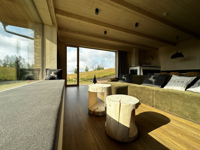 Přírodní minimalistický design a decentní barevná paleta zajišťuje dokonalou eleganci. Velkými okny proudí dovnitř mnoho světla, přes které je možné pozorovat malebnou krajinu, která celou chatu obklopuje. Fasádu domu tvoří ručně štípané modřínový šindel, zatímco uvnitř je obloženo smrkovými biodeskami.
