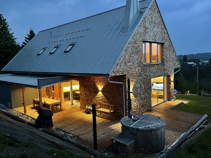Přírodní minimalistický design a decentní barevná paleta zajišťuje dokonalou eleganci. Velkými okny proudí dovnitř mnoho světla, přes které je možné pozorovat malebnou krajinu, která celou chatu obklopuje. Fasádu domu tvoří ručně štípané modřínový šindel, zatímco uvnitř je obloženo smrkovými biodeskami.
