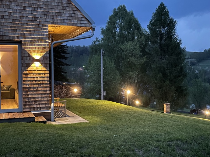 Přírodní minimalistický design a decentní barevná paleta zajišťuje dokonalou eleganci. Velkými okny proudí dovnitř mnoho světla, přes které je možné pozorovat malebnou krajinu, která celou chatu obklopuje. Fasádu domu tvoří ručně štípané modřínový šindel, zatímco uvnitř je obloženo smrkovými biodeskami.
