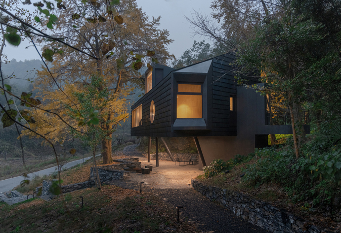 Architekti z Moguang Studio postavili mezi stromy chatu, která neruší, ale přirozeně splyne s lesem. Dům stojí na pilířích, aby nepoškodil kořeny starých stromů, a místo klasických oken má geometrické výřezy, které rámují krajinu.
