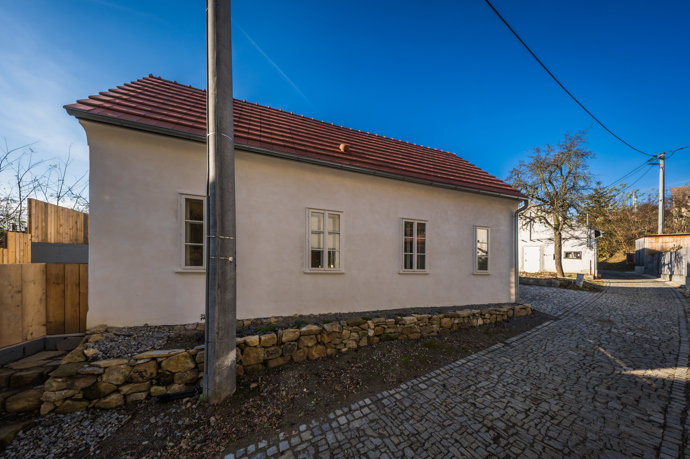Už když otevřete vrátka, máte pocit, jako byste vstoupili do malované pohádky. Malý bílý domek s kouzelnými detaily, dřevěné trámy, květiny v oknech, klid a žádný spěch. Interiér voní dřevem a poctivou řemeslnou prací, ale nese v sobě i moderní komfort. A co je možná nejdůležitější – všechno tu působí opravdově a srdečně. 

