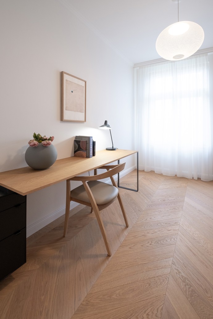 Bílé stěny a nábytek na míru vytvářejí neutrální kulisu, ve které mohou vyniknout jak původní architektonické prvky – například zdobné okenní rámy a vysoké stropy –, tak i umělecké detaily, jako jsou historické obrazy.
