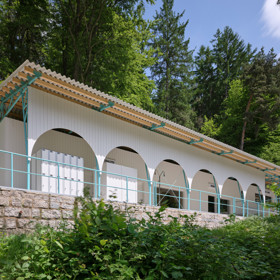 Návrh vypracovalo architektonické studio Mjölk architekti a zahrnovalo například kombinaci CLT konstrukce s lehkým dřevěným rámem, lehké trámkové konstrukce, a to vše pod tyrkysovou střechou, která slouží jako ochrana i stínidlo. Když na ni padne odpolední světlo, odráží se od ní paprsky jako od vodní hladiny. 
