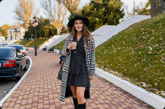 Černé šaty s bílým vzorem působí elegantně a univerzálně. Vysoké kozačky outfit dělají modernějším a zároveň praktickým pro chladné počasí. Klobouk dodává francouzský šmrnc. Vzorovaný kabát pak celý look oživuje a přináší zajímavý prvek navíc. Výsledkem je šik kombinace.
