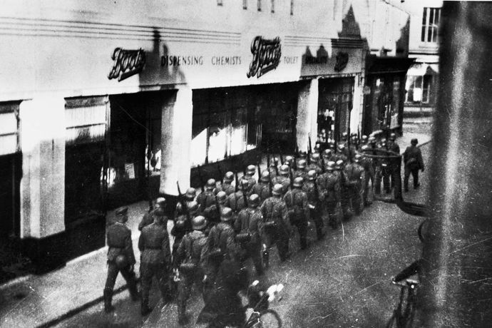 Němečtí vojáci pochodují před lékárnou na Normanských ostrovech, 40. léta 20. století. Claude Cahun se spolu se svou partnerkou Marcel Moore účastnila protinacistického odboje.
Němečtí vojáci pochodují před lékárnou na Normanských ostrovech, 40. léta 20. století. Claude Cahun se spolu se svou partnerkou Marcel Moore účastnila protinacistického odboje.