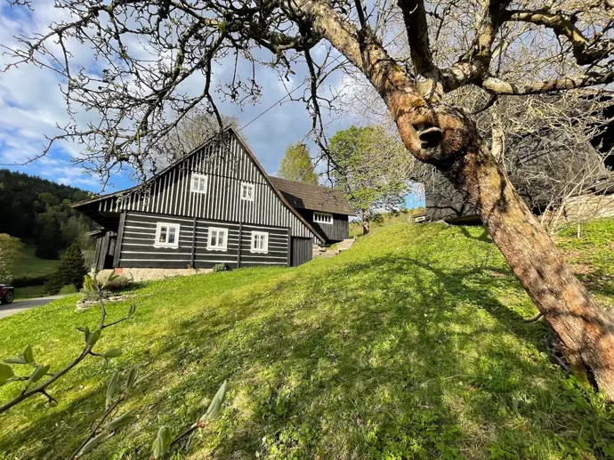 Pohled na roubenku zvenčí ukazuje, jak přirozeně zapadá do okolní krajiny a venkovského prostředí.
