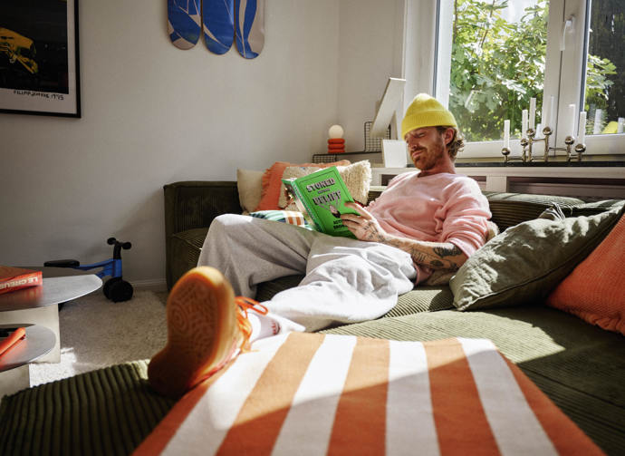 Koutek doplňuje zelená lampa na zrcadlovém stolku a koberec s bílým podkladem a barevnými prvky. 
