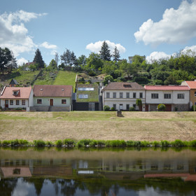 Pozemek, na kterém stojí tento jedinečný domek s travnatou střechou, je prolukou mezi rodinnými domy, které tvoří nábřeží řeky Dyje. Terén pozemku je velmi svažitý, má původní terasovou úpravu s kamennými stěnami. 
