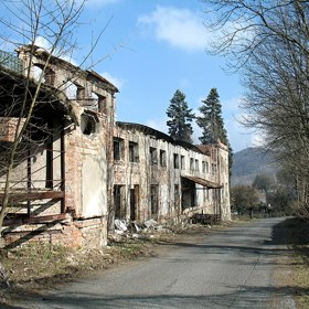 Na první pohled působí spíš jako kulisa z postapokalyptického filmu. Oprýskané zdi, propadlé střechy a zdevastované interiéry. Přesto, když se postavíte před hlavní budovy někdejší sklárny, které místní neřeknou jinak než Eliáška a zavřete oči, můžete téměř slyšet, jak se tu asi kdysi žilo a vyrábělo.
