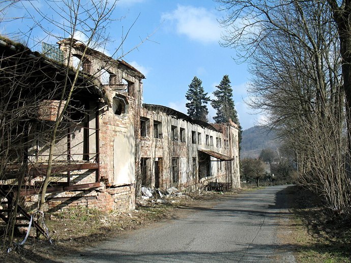 Na první pohled působí spíš jako kulisa z postapokalyptického filmu. Oprýskané zdi, propadlé střechy a zdevastované interiéry. Přesto, když se postavíte před hlavní budovy někdejší sklárny, které místní neřeknou jinak než Eliáška a zavřete oči, můžete téměř slyšet, jak se tu asi kdysi žilo a vyrábělo.
