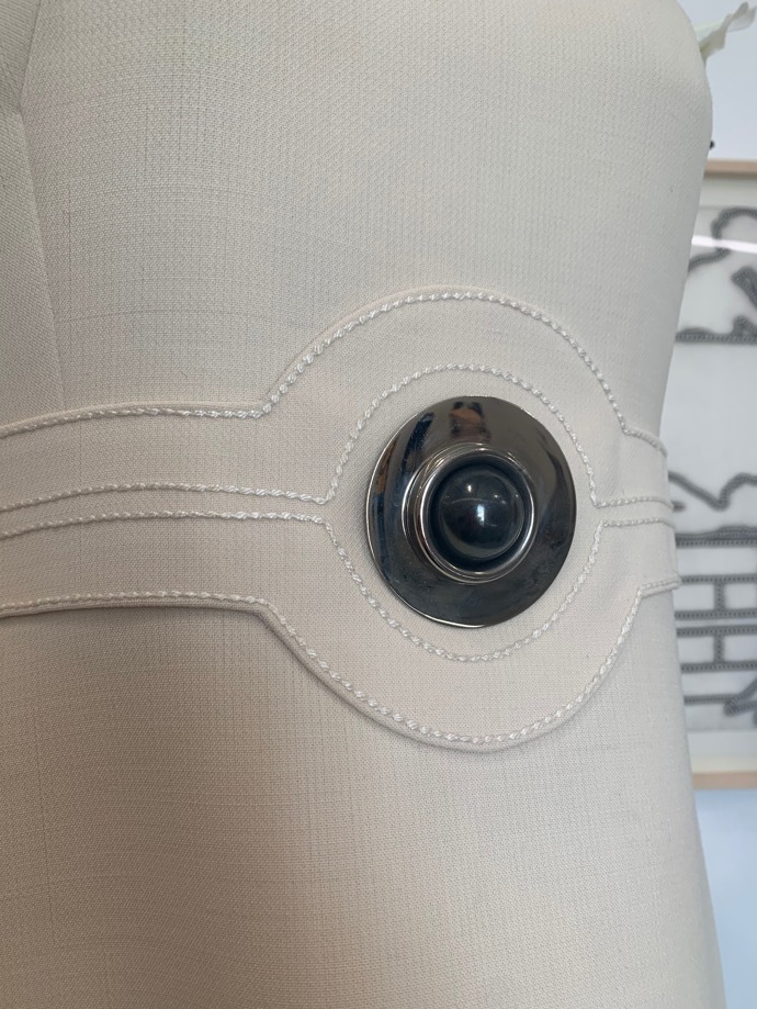 Detail šatů s kovovými prvky.