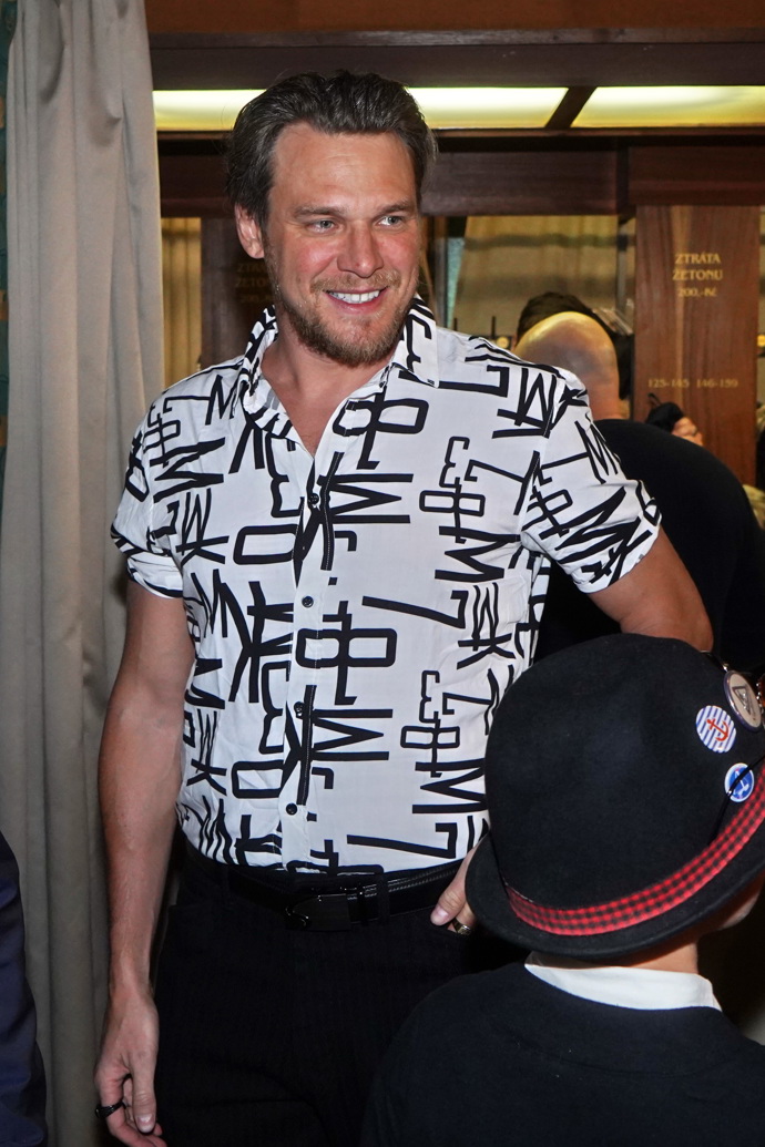 Herec Vojtěch Dyk přišel do Lucerny v bílé košili s černým potiskem a černých společenských kalhotách.