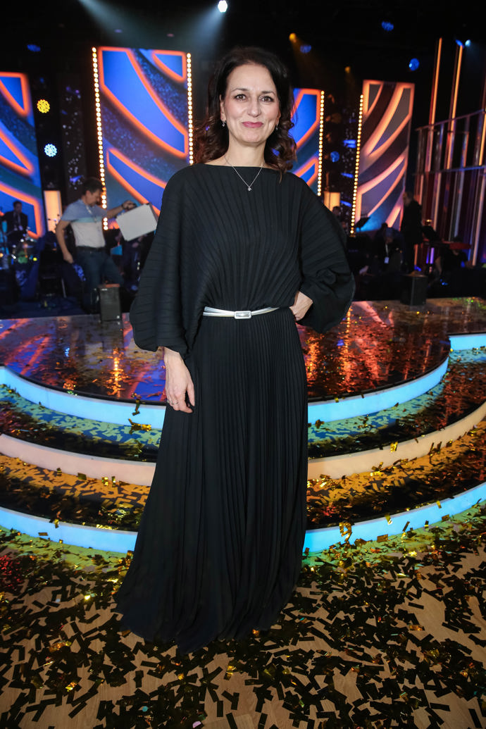 Zlatý doplněk rozzářil i jinak celočerné plisované večerní šaty s výraznými rukávy.