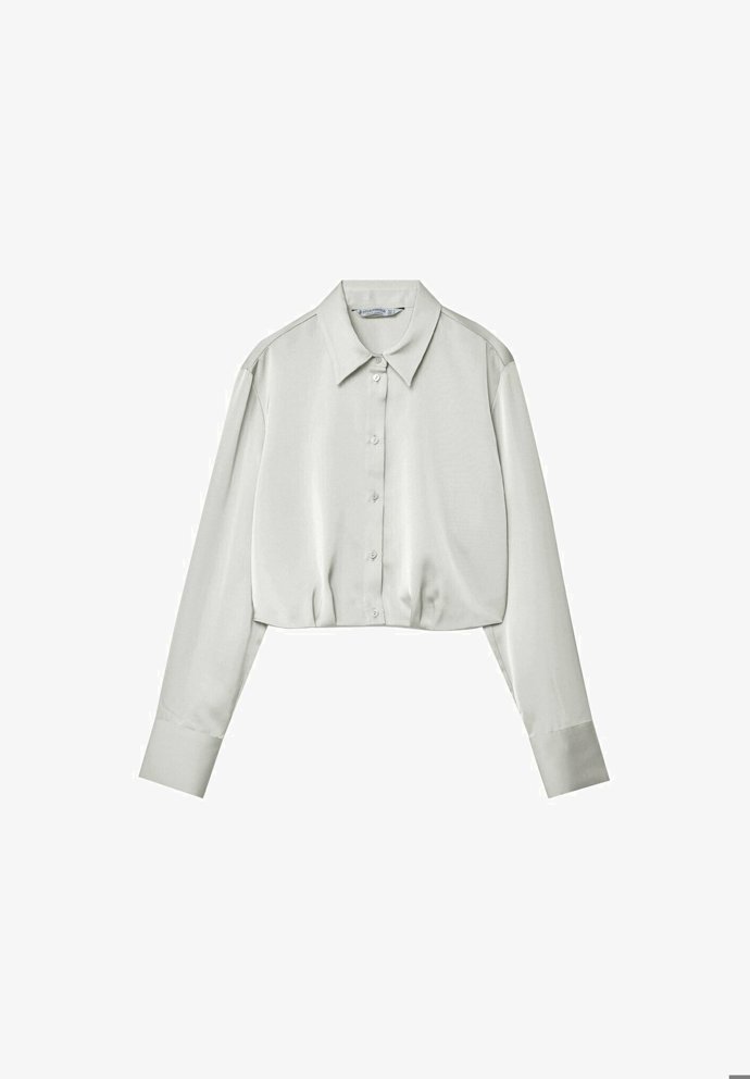 Saténovou blůzu zkráceného střihu v neutrálním tónu a mnoha dalších barevných provedeních nabízí  Stradivarius za 549 Kč.