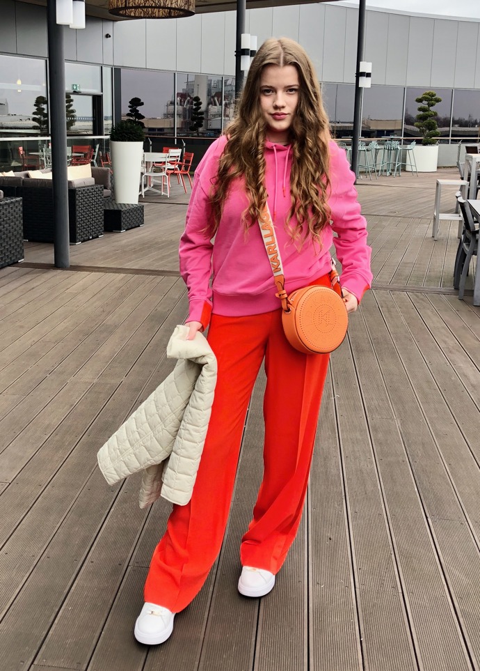 První dámský outfit inklinuje ke sportovně elegantnímu stylu. Vévodí mu výrazná oranžová a růžová barva.