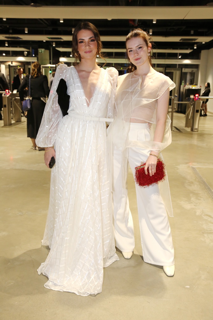 Herečka Sára Korbelová (vpravo) oblékla v roce 2024 transparentní bílý top a bílé kalhoty, to celé doplněné o výrazné rudé psaníčko.