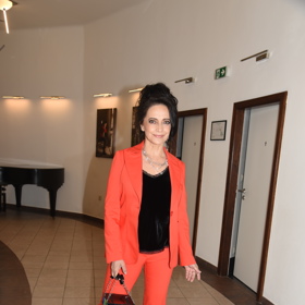 Zpěvačka Lucie Bílá kombinuje cihlově červené cigaretové kalhoty s černým topem.