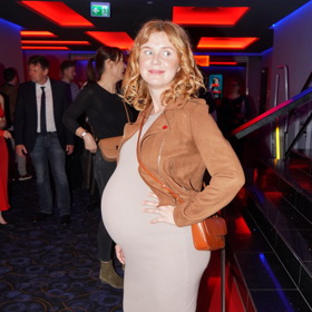 Herečka Martina Babišová ve vysokém stupni těhotenství obléká pohodlné béžové šaty z pleteniny doplněné o hnědou koženou bundičku do pasu a hnědé kovbojské kozačky. 