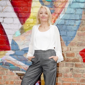 Veronika Žilková v šedivých kalhotách s vysokým pasem z dílny Martiny Pipkové Loudové. Doplnila je bílou košilí a bílým topem.