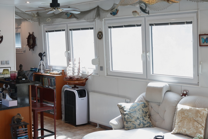 V obývací části hausbótu je světlo díky velkým oknům, která jsou ve směru od břehu chráněna fóliemi. Ty poskytují obyvatelům hausbótu dostatek soukromí.