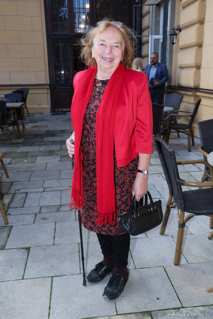 Livia Klausová oblékla červené sáčko i šál a černo-červené šaty doplněné o černou koženou kabelku. Pohodlné černé tenisky jsou pochopitelnou volbou vzhledem k věku bývalé první dámy i místu konání akce. 