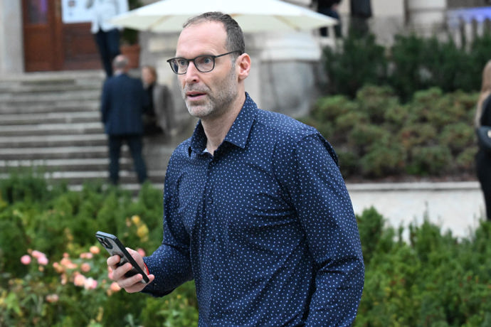 Elegantní košile a kalhoty kontrastovaly s jeho unaveným vzhledem.