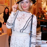 K bílým koktejlkám nosí modelka černý klobouk s užší krempou.