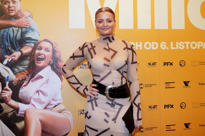 Přes světlé šaty s potiskem a stojáčkem nosí široký pásek herečka Erika Stárková.