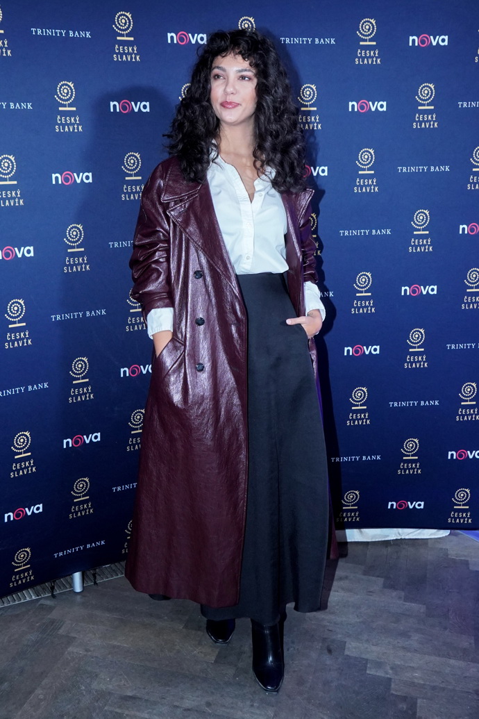 Zea oblékla bílou halenku a černou sukni s vysokým pasem, přes to dlouhý vínový kabát. 