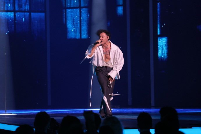 ...a ve volné bílé košili s vázačkami na rukávech, kalhotách s ladícími detaily a třpytivém tílku s proklatě hlubokým výstřihem zazpíval a odhalil svůj potetovaný hrudník.