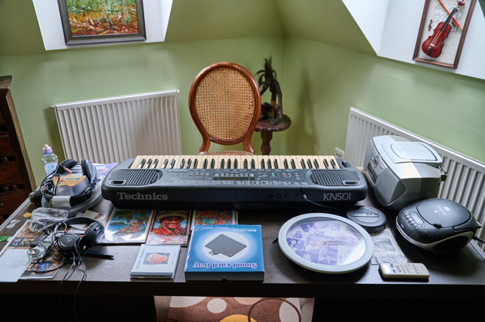 Pracovní stůl v hudebním pokoji ze zavalený věcmi.