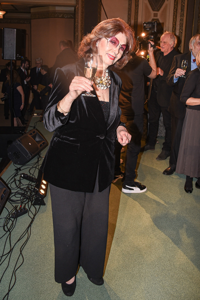 Moderátorka Kalendária oblékla své oblíbené sametové sako a široké kalhoty. Nechybí její ikonické brýle. 