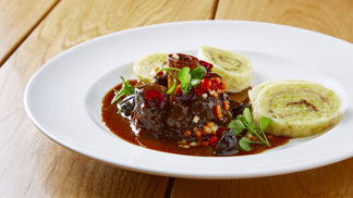 Jelení Ossobuco s pivní omáčkou, bramborovými knedlíky s perníkem, brusinkami a jeřabinami podle šéfkuchaře Lukáše Holého
Suroviny:
Jelení Ossobuco
4 plátky jeleních kolínek
olivový olej
drcený jalovec
pepř, sůl
Pivní omáčka
125 g másla
8 šalotek
250 g směsi kořenové zeleniny
80 g cukru
výpek z masa
0,5 l černého piva OSSEGG
100 ml masového či zeleninového vývaru
2 stroužky česneku
4 lžičky tymiánu
2 lžičky rozmarýnu
pepř, sůl
Bramborové knedlíky s perníkem
700 g vařených brambor
200 g hrubé mouky
1 vejce
sůl
100 g perníku na strouhání
50 ml slunečnicového oleje
Brusinky
100 g sušených brusinek
100 ml červeného vína
30 g cukru
hvězdička badiánu
celá skořice
Jeřabiny
jeřabiny v sladkokyselém nálevu
pivovice Svach
Máslová kořenová zelenina
200 g kořenové zeleniny (mrkev, celer, petržel)
olivový olej
Postup:
Jelení Ossobuco: vytvoříme marinádu ze směsi koření, pepře, soli, drceného jalovce a oleje. Směs pečlivě vmasírujme do masa a necháme marinovat alespoň 12 hodin. Pro podávání maso zprudka opečeme na oleji na rozehřáté pánvi.
Pivní omáčka: kořenovou zeleninu nakrájíme na kostičky, šalotku nakrájíme najemno. Na másle opečeme zeleninu, přidáme šalotku. Když je vše dozlatova opečené, přidáme výpek z masa, poté zalijeme černým pivem a vývarem, přidáme drcený česnek a bylinky a vaříme na mírném ohni alespoň 20 minut.
Do připraveného základu omáčky vložíme na pánvi opečené maso a při nízké teplotě dusíme doměkka. Potom maso vyjmeme a pivní omáčku propasírujeme a dále sváříme na požadovanou hustotu. Když máme svařeno, přidáme vychlazené máslo, sundáme ze sporáku a máslo zašleháme. Hotovou pivní omáčku ještě dochutíme solí.
Bramborové knedlíky s perníkem: z uvařených brambor, mouky, vejce a soli vypracujeme těsto. To pak vyválíme do tenkého plátu, potřeme štětcem připravenou směsí oleje a najemno nastrouhaného perníku. Těsto zarolujeme a upravíme do tvaru knedlíku. Knedlíky vaříme v páře 28 minut. Po uvaření knedlíky potřeme máslem nebo sádlem, krájíme a servírujeme
Brusinky: sušené brusinky vaříme ve víně s cukrem a kořením na mírném ohni alespoň 10 min, potom brusinky s kořením scedíme a zbylou šťávu svaříme na polovinu. Nakonec do šťávy vrátíme povařené brusinky.
Jeřabiny: nakládané jeřabiny marinujeme několik dnů v alkoholu.
Máslová kořenová zelenina: zeleninu nakrájíme na malé kostičky a orestujeme na pánvi na másle na zkus a dochutíme solí a pepřem.
Servírování
Plátek ossobuco zdobíme na talíři máslovou kořenovou zeleninou, přidáme brusinky a jeřabiny a spolu s perníkovými knedlíky přelijeme pivní omáčkou.