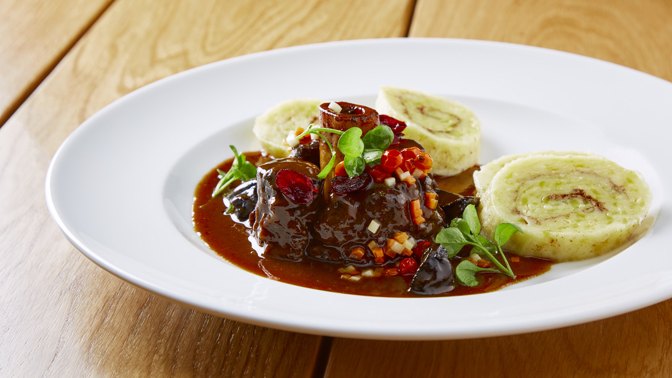 Jelení Ossobuco s pivní omáčkou, bramborovými knedlíky s perníkem, brusinkami a jeřabinami podle šéfkuchaře Lukáše Holého
Suroviny:
Jelení Ossobuco
4 plátky jeleních kolínek
olivový olej
drcený jalovec
pepř, sůl
Pivní omáčka
125 g másla
8 šalotek
250 g směsi kořenové zeleniny
80 g cukru
výpek z masa
0,5 l černého piva OSSEGG
100 ml masového či zeleninového vývaru
2 stroužky česneku
4 lžičky tymiánu
2 lžičky rozmarýnu
pepř, sůl
Bramborové knedlíky s perníkem
700 g vařených brambor
200 g hrubé mouky
1 vejce
sůl
100 g perníku na strouhání
50 ml slunečnicového oleje
Brusinky
100 g sušených brusinek
100 ml červeného vína
30 g cukru
hvězdička badiánu
celá skořice
Jeřabiny
jeřabiny v sladkokyselém nálevu
pivovice Svach
Máslová kořenová zelenina
200 g kořenové zeleniny (mrkev, celer, petržel)
olivový olej
Postup:
Jelení Ossobuco: vytvoříme marinádu ze směsi koření, pepře, soli, drceného jalovce a oleje. Směs pečlivě vmasírujme do masa a necháme marinovat alespoň 12 hodin. Pro podávání maso zprudka opečeme na oleji na rozehřáté pánvi.
Pivní omáčka: kořenovou zeleninu nakrájíme na kostičky, šalotku nakrájíme najemno. Na másle opečeme zeleninu, přidáme šalotku. Když je vše dozlatova opečené, přidáme výpek z masa, poté zalijeme černým pivem a vývarem, přidáme drcený česnek a bylinky a vaříme na mírném ohni alespoň 20 minut.
Do připraveného základu omáčky vložíme na pánvi opečené maso a při nízké teplotě dusíme doměkka. Potom maso vyjmeme a pivní omáčku propasírujeme a dále sváříme na požadovanou hustotu. Když máme svařeno, přidáme vychlazené máslo, sundáme ze sporáku a máslo zašleháme. Hotovou pivní omáčku ještě dochutíme solí.
Bramborové knedlíky s perníkem: z uvařených brambor, mouky, vejce a soli vypracujeme těsto. To pak vyválíme do tenkého plátu, potřeme štětcem připravenou směsí oleje a najemno nastrouhaného perníku. Těsto zarolujeme a upravíme do tvaru knedlíku. Knedlíky vaříme v páře 28 minut. Po uvaření knedlíky potřeme máslem nebo sádlem, krájíme a servírujeme
Brusinky: sušené brusinky vaříme ve víně s cukrem a kořením na mírném ohni alespoň 10 min, potom brusinky s kořením scedíme a zbylou šťávu svaříme na polovinu. Nakonec do šťávy vrátíme povařené brusinky.
Jeřabiny: nakládané jeřabiny marinujeme několik dnů v alkoholu.
Máslová kořenová zelenina: zeleninu nakrájíme na malé kostičky a orestujeme na pánvi na másle na zkus a dochutíme solí a pepřem.
Servírování
Plátek ossobuco zdobíme na talíři máslovou kořenovou zeleninou, přidáme brusinky a jeřabiny a spolu s perníkovými knedlíky přelijeme pivní omáčkou.