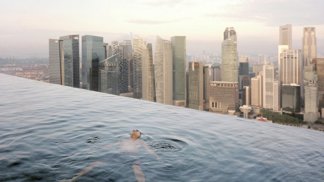 Muž plave v „nekonečném bazénu“ na střeše Marina Bay Sands Hotel.