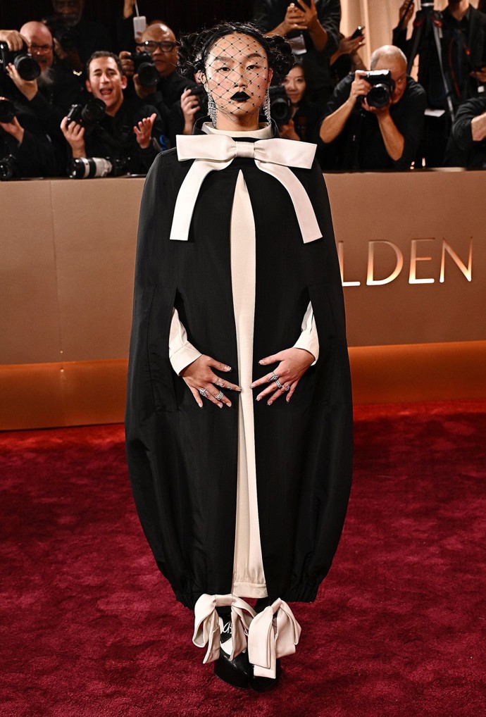 Zpěvačka Audrey Nuna tomu nasadila korunu, když na červený koberec dorazila v černobílém dlouhatánském kokonovitém saku z podzimní kolekce 2024 návrhářů Thoma Brownea a Valdrina Sahitiho. Výstřední krejčovský kousek navíc zdobila obří mašle u krku a další dvě u kotníků.