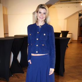 Modelka oblékla tmavě modrý komplet širokých kalhot s vysokým pasem a propínacího svetříku se zlatými knoflíky. 