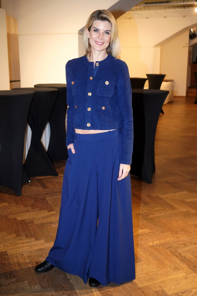 Modelka oblékla tmavě modrý komplet širokých kalhot s vysokým pasem a propínacího svetříku se zlatými knoflíky. 