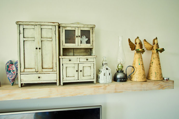 Nad televizí je jednoduchá polička s drobnými dekoracemi a osobními předměty.