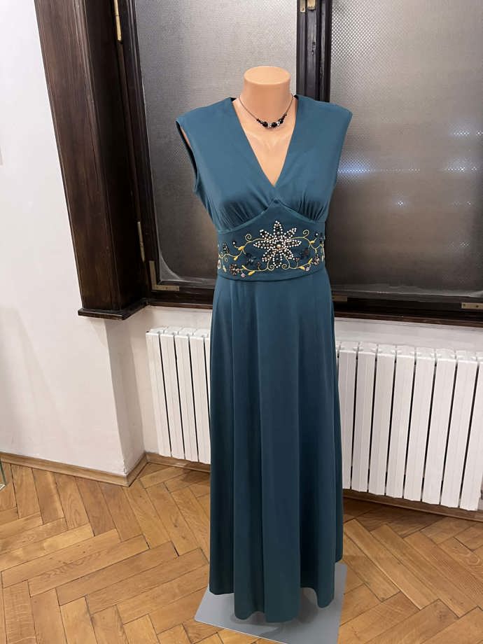 Modrozelené petrolejové šaty mají povážlivě hluboký výstřih. 