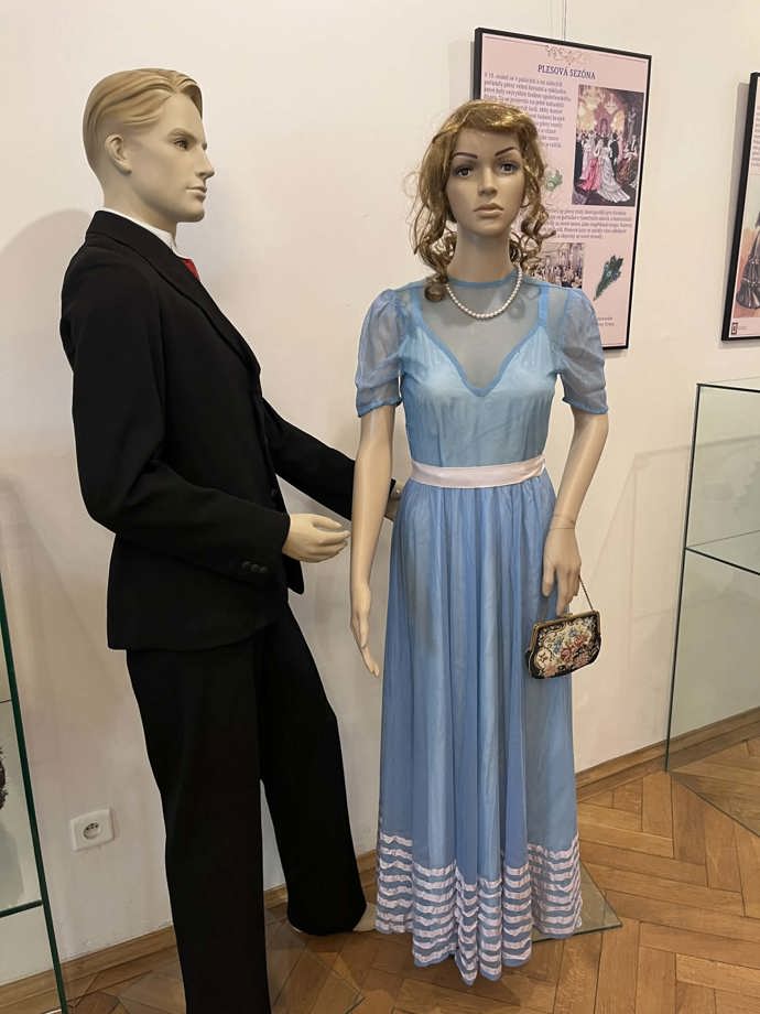 Pastelově modrá róba, doplněná perlovým náhrdelníkem. 