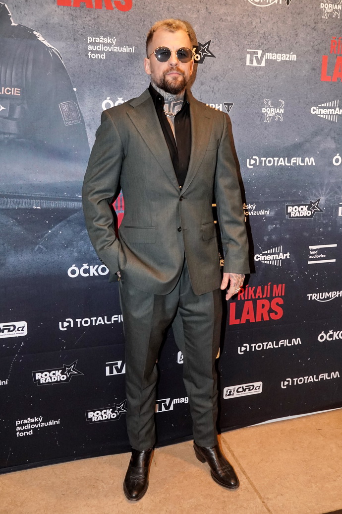 Marpo pózoval u fotostěny v tmavě šedém obleku a černé rozhalené košili. 