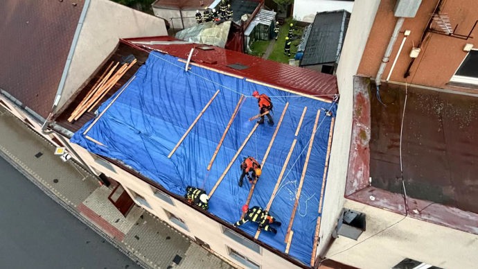 Provizorní zajištění poškozené střechy pomocí plachty, aby do obytných prostor dál nezatékalo.