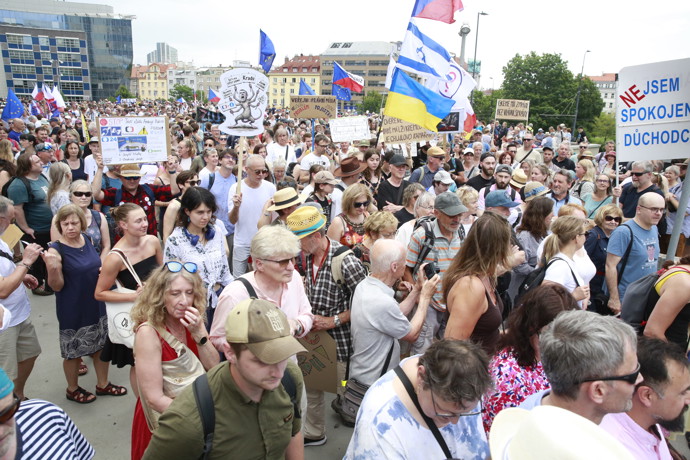 Pohled do zaplněného davu demonstrantů nesoucích různé transparenty a státní vlajky.