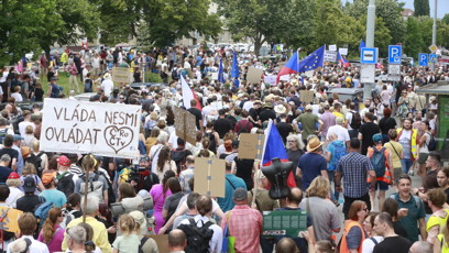 FOTO: Průvod nespokojených občanů s transparenty a vlajkami se pohybuje po silnici během protestní akce.