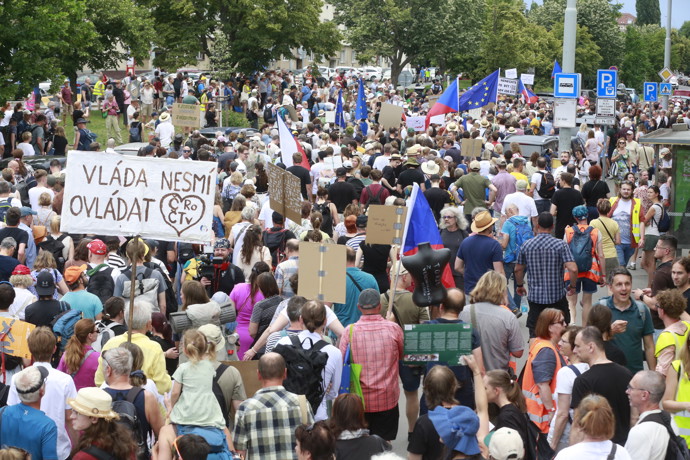 Průvod nespokojených občanů s transparenty a vlajkami se pohybuje po silnici během protestní akce.