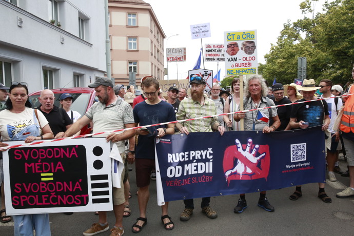 Demonstranti v čele průvodu drží velký tmavý transparent vyzývající k ochraně veřejné služby.