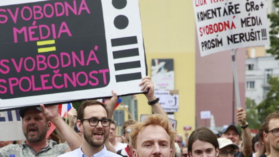 FOTO: Detailní záběr na skupinu účastníků pochodujících s transparenty v předních řadách demonstrace.