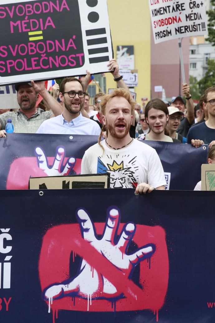 Detailní záběr na skupinu účastníků pochodujících s transparenty v předních řadách demonstrace.